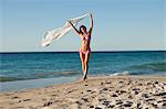 Young beautiful woman walking on the beach while holding her sarong in the air