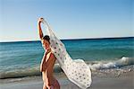 Portrait of an attractive woman holding her sarong in the air with the ocean in background