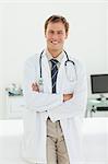 Smiling male doctor with arms crossed standing in his examination room