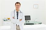 Male doctor with his arms folded standing in his examination room