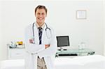 Smiling male doctor with his arms folded in his examination room