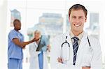 Smiling doctor with arms folded and two colleagues behind him