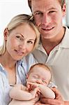 Close up of smiling mother and father with their baby against a white background