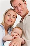 Close up of smiling parents with their baby against a white background
