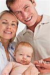 Close up of smiling parents with their little baby against a white background
