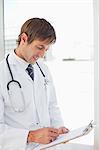 Smiling doctor working with his clipboard while standing in front of a window