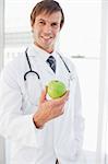 A surgeon is holding a green apple in front of a window