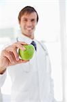 A smiling surgeon is holding a delicious green apple in front of a window