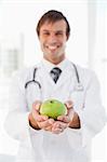 A happy doctor is holding a green apple in front of a window