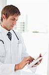 Serious doctor using his tablet pc in front of a window