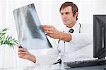 Médecin sérieux tout en restant assis à son bureau derrière son ordinateur en regardant une radiographie