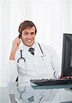 Doctor talking on his mobile phone while smiling and sitting at his desk