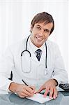 Smiling surgeon writing a prescription on his desk while looking at the camera