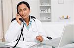 Serious doctor looking at the camera while talking on the phone in her medical office