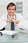 Doctor with a stethoscope placing his elbows on the desk while smiling