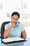 Young serious secretary looking at a binder folder while sitting at a desk