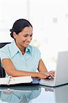 Smiling secretary working with a laptop while sitting at a desk in a bright room