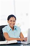 Happy secretary using her laptop while sitting at a desk and staring at the camera