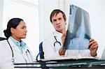 Serious surgeons sitting at a desk side by side while talking about a chest x-ray