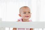 Beau bébé regardant vers le côté tout en souriant et debout dans son lit