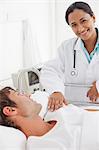 Smiling doctor looking at the camera while standing next to her patient lying in a bed