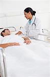 Serious doctor standing next to the bed of a patient while holding his shoulder