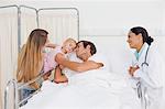 Patient lying in a hospital bed while hugging her baby and being looked by a doctor