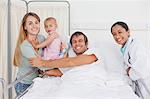 Smiling family and a doctor looking at the camera while staying in a hospital room