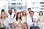 A group of colleagues look ahead and applaud as they sit next to each other