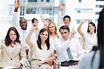 A group of colleagues raising their arms while watching a speaker