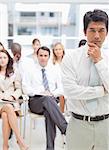 Serious businessman looking ahead of him as he holds his chin in his hands while standing in front of his colleagues