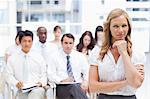 Businesswoman looking ahead of her while resting her chin on her hand as she stands in front of her colleagues