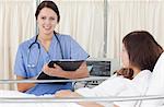 Smiling nurse looking in front of her while holding a clipboard next to the bed of a patient