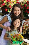 Mother with daughter holding young flowers in plant nursery, portrait