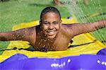 Boy (10-12) Sliding on water slide, front view portrait.