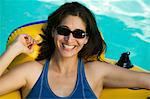 Woman wearing sunglasses, lying on inflatable raft in swimming pool, portrait.
