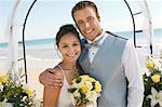 Bride and Groom under archway on beach, (portrait)