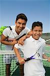 Father and son standing at net on tennis court, portrait