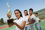 Tennis Family on court by net, daughter holding trophy, portrait