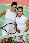 Mother and daughter standing at net on tennis court, portrait, high angle view