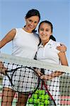 Mother and daughter standing at net on tennis court, portrait, low angle view
