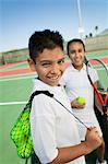 Young boy and girl with tennis equipment on tennis court, focus on boy, portrait