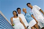 Four mixed doubles tennis players at net on tennis court, portrait, low angle view