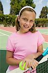 Young girl with tennis racket and ball by net at tennis court, portrait