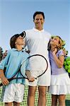 Father with Son and Daughter by net on Tennis Court, portrait, front view