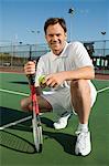 Homme accroupi sur le Court de Tennis, raquette de tennis et balle, portrait