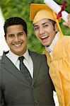 Graduate hoisting diploma with arm around father outside, portrait