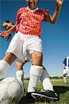 Girls (13-17) playing soccer, one tackling another, low angle view, cropped