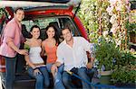 Two young couples sitting in open car trunk in garden centre, (portrait)