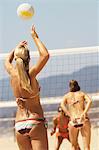 Female beach volleyball player serving volleyball, back view